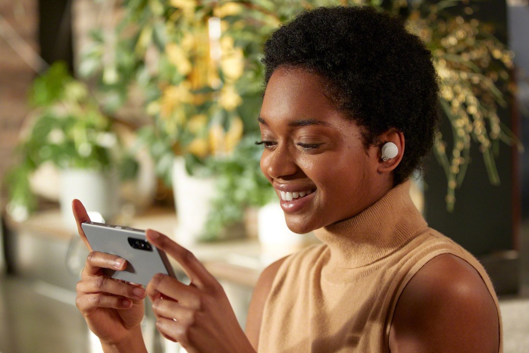 A woman holds a smartphone and listens to Sony wireless earbuds