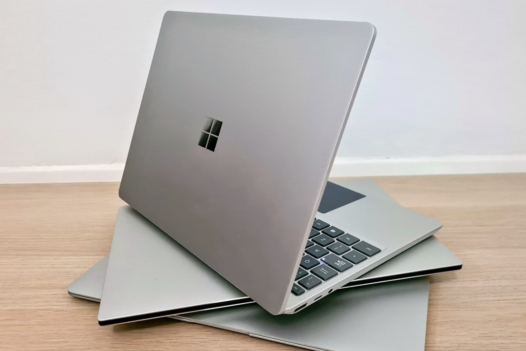 An open laptop with a Microsoft logo sits on top of more laptops