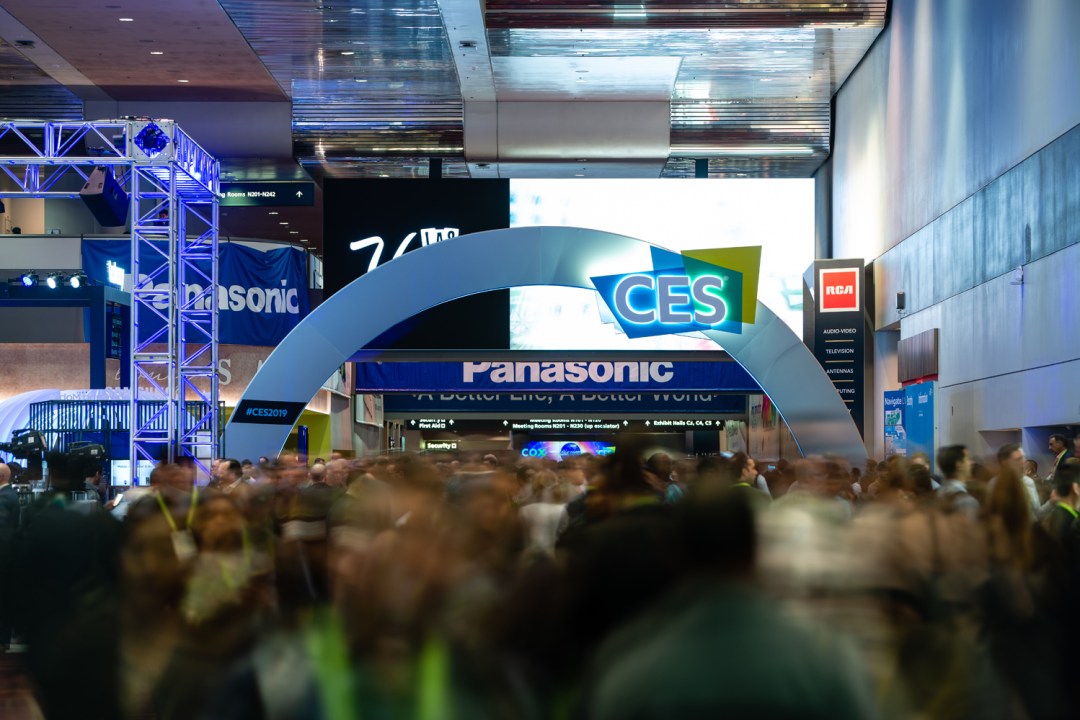 A crowd of people walking by an arch with the CES logo on it
