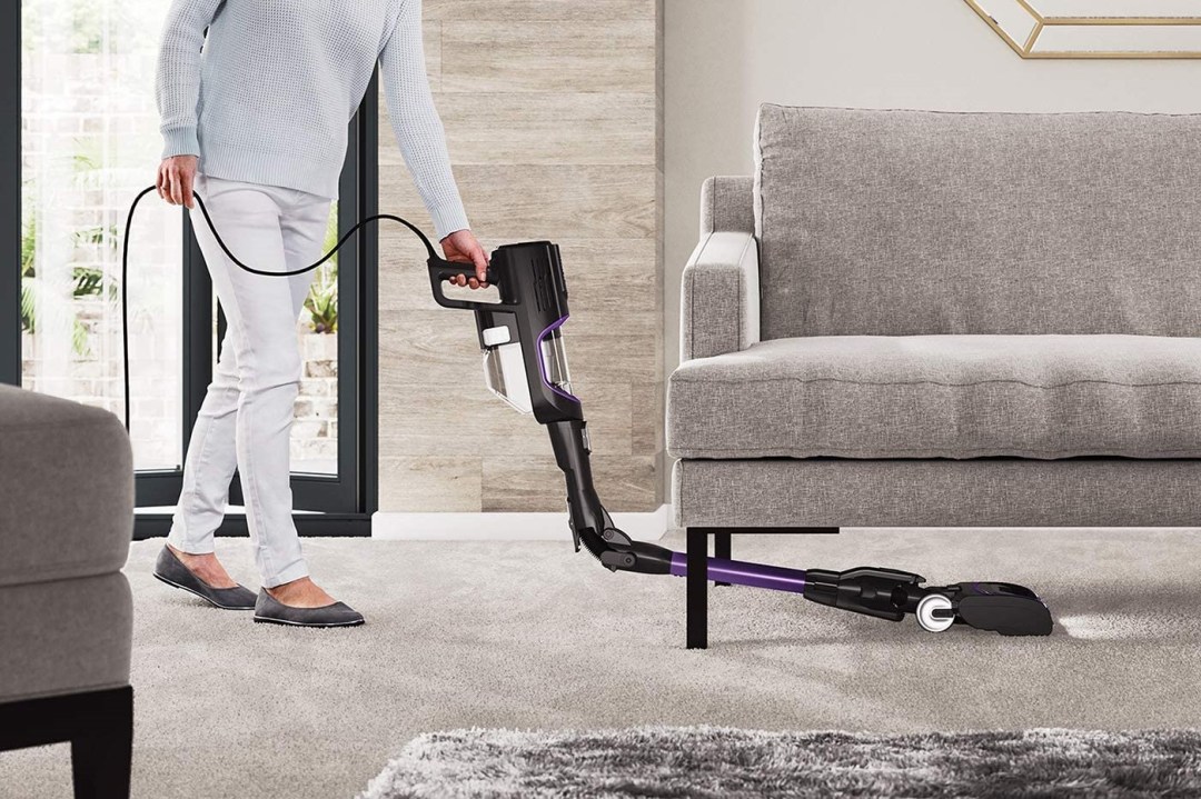 A vacuum cleaner being used to clean under a sofa
