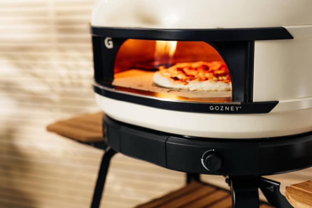 Gozney Dome S1 pizza oven with flames and a pizza visible inside.