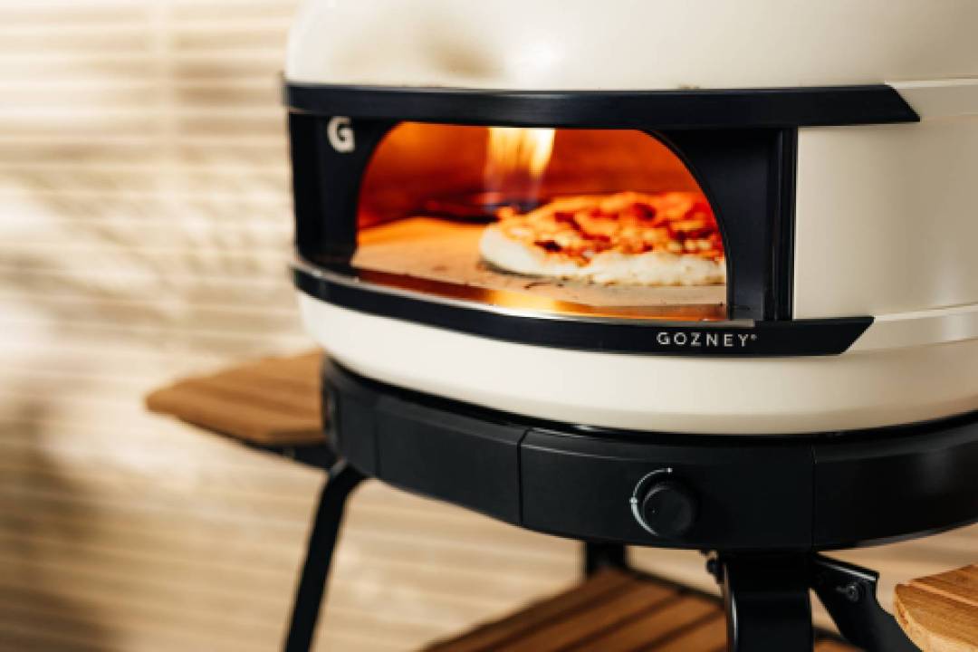 Gozney Dome S1 pizza oven with flames and a pizza visible inside.