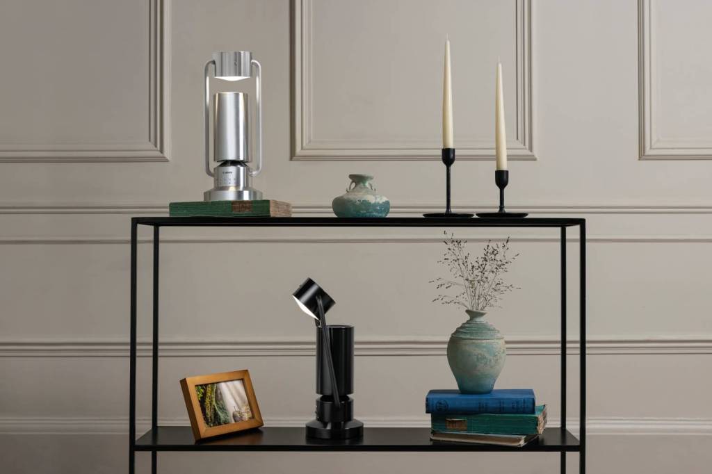 Two Canon Light & Speaker ML-A on a furniture unit that also contains candles, books, a picture frame and two vases.