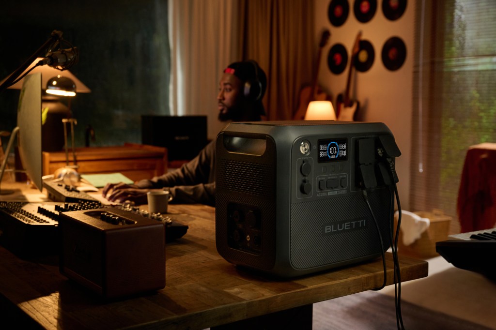 A man works at an iMac with a Bluetti power station in the foreground