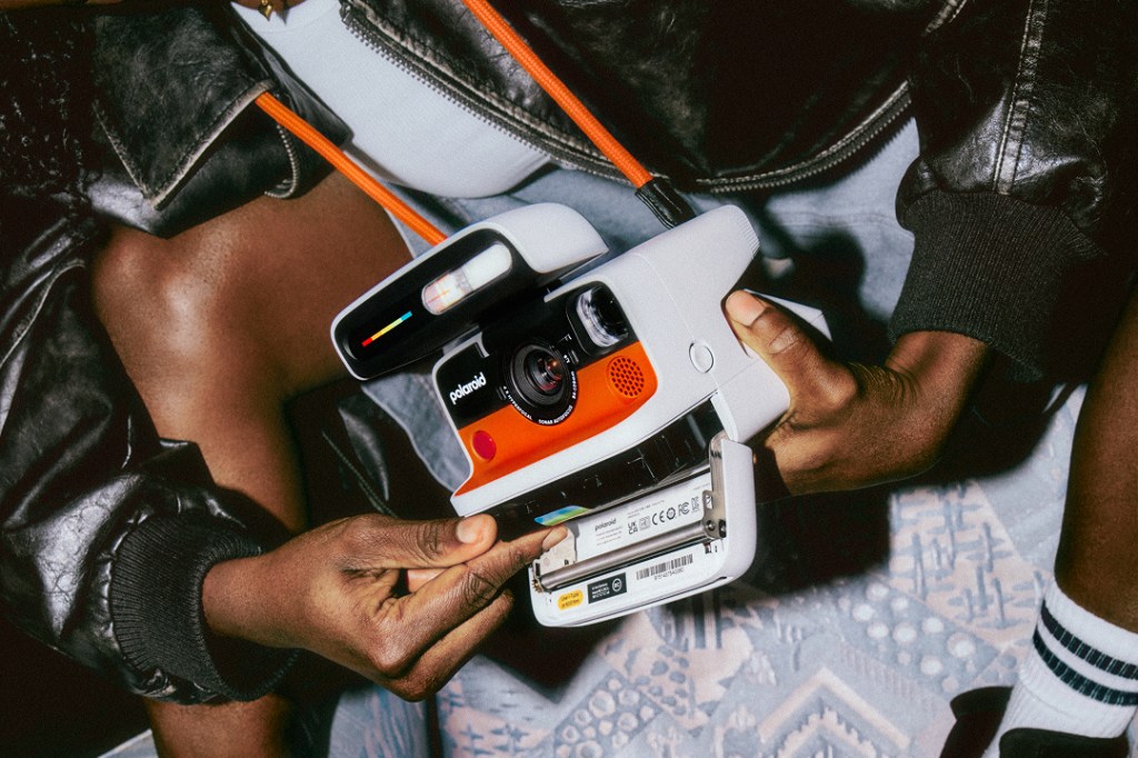 Somebody holding a Polaroid Flip camera with the flap at the bottom opened to access the film