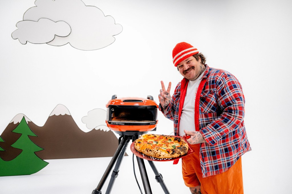 The Matty Matheson Signature Tread pizza oven on cartoon background with Matty standing beside it