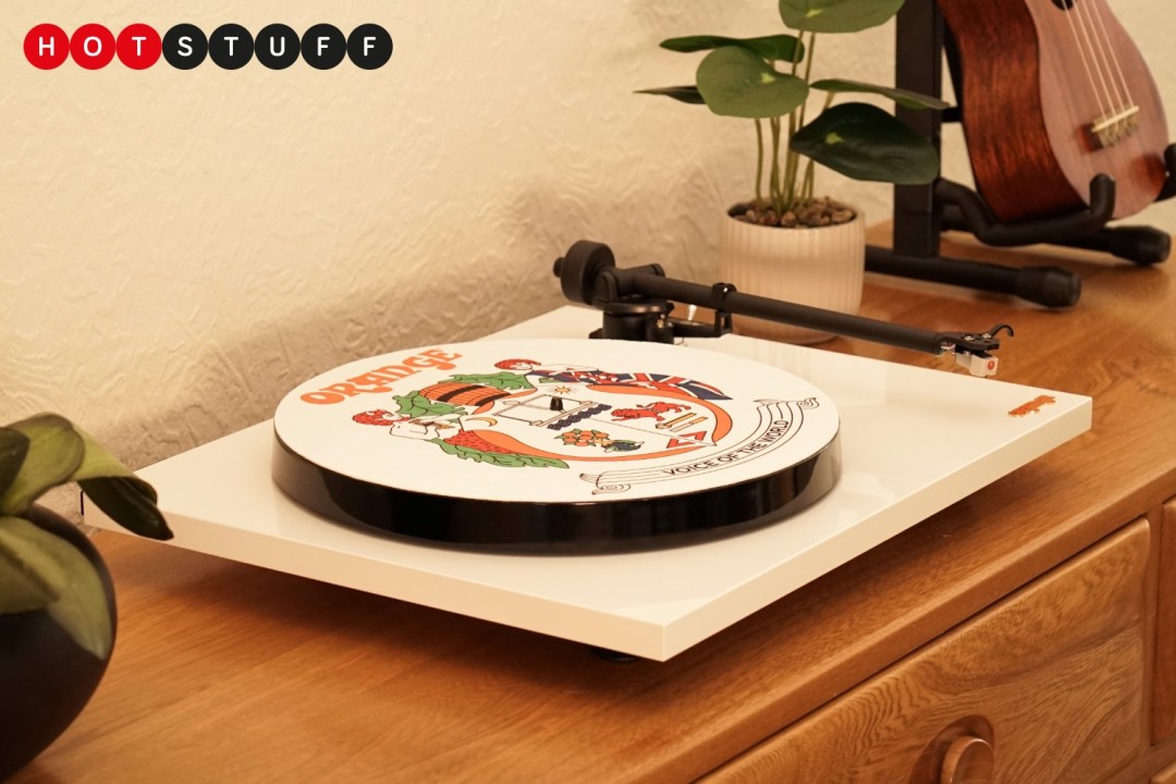 An Orange Amps O Turntable on a wooden sideboard. There are plants visible in the background.