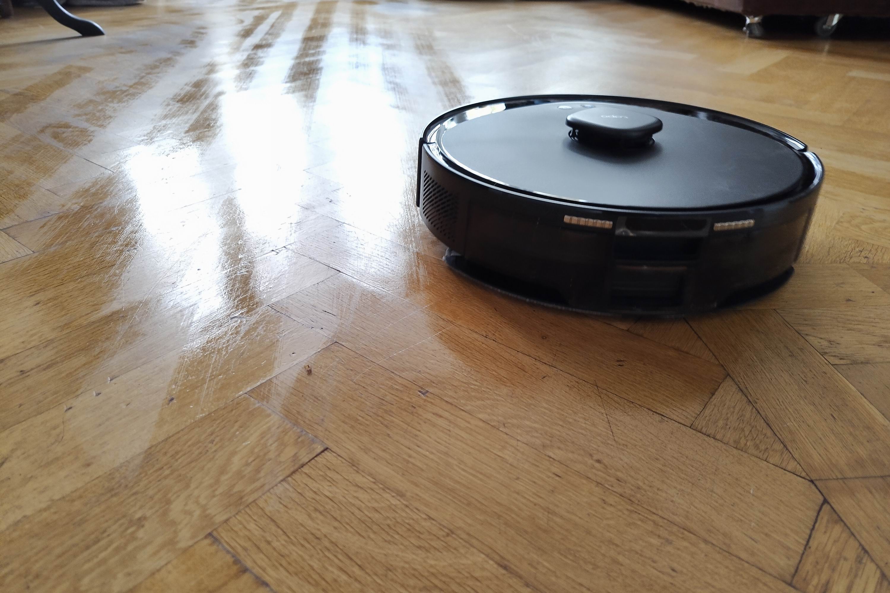 A robot vacuum on a shiny, mopped wooden floor