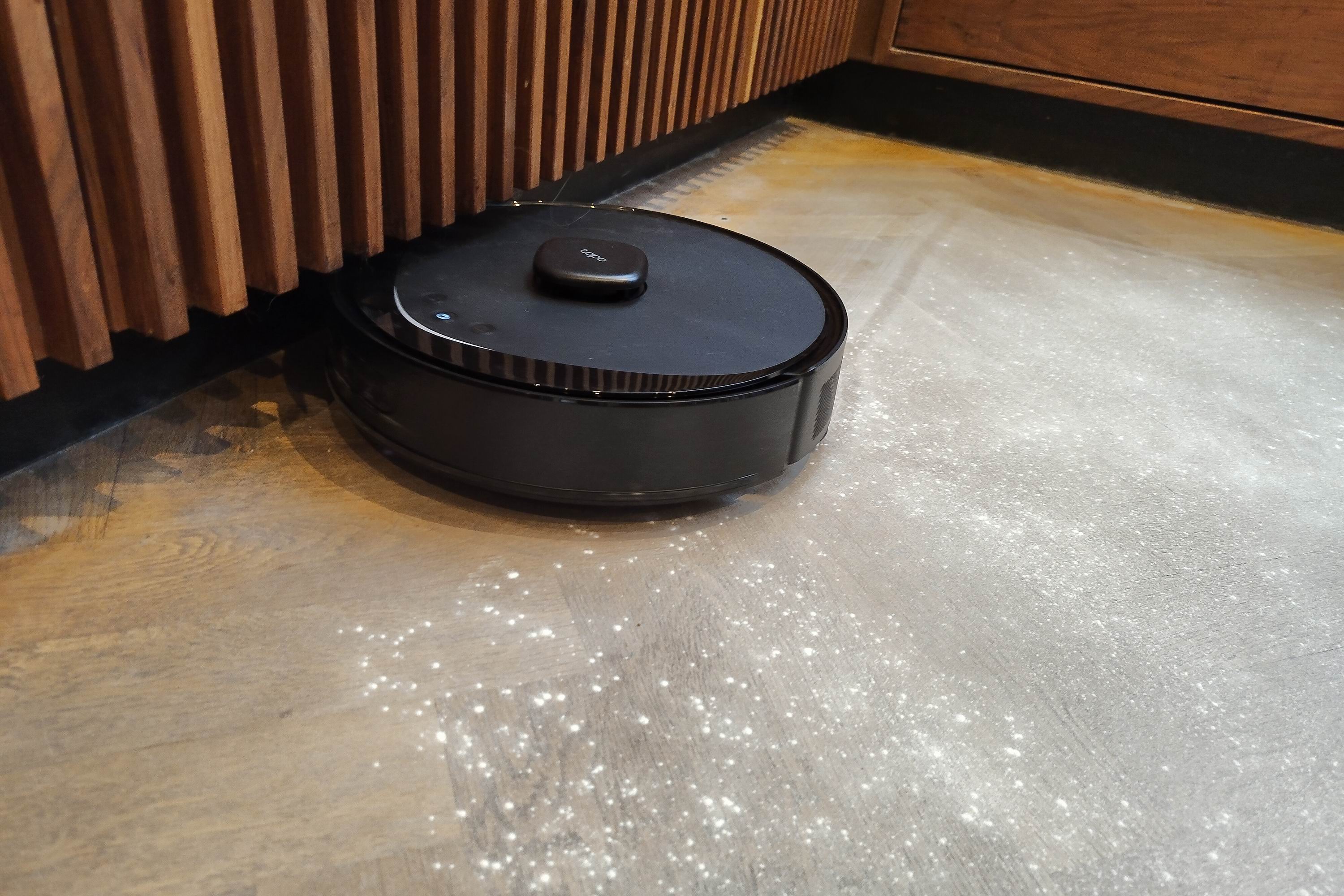 A robot vacuum cleans under the front of kitchen cupboards